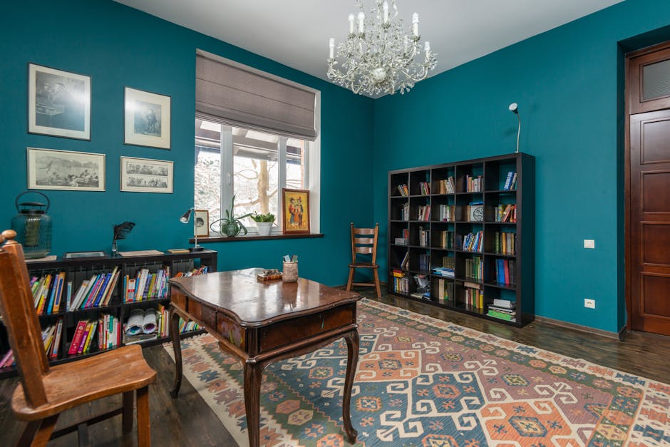 Vintage styled room with wooden chair at table placed on carpet near books on shelves at blue walls and window